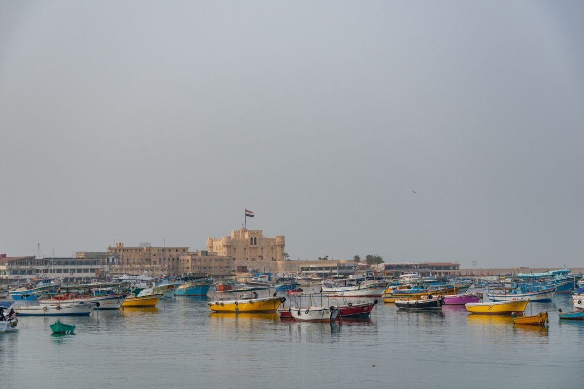 Colorful boats float in Alexandria’s harbor with the historic Citadel of Qaitbay in the background.