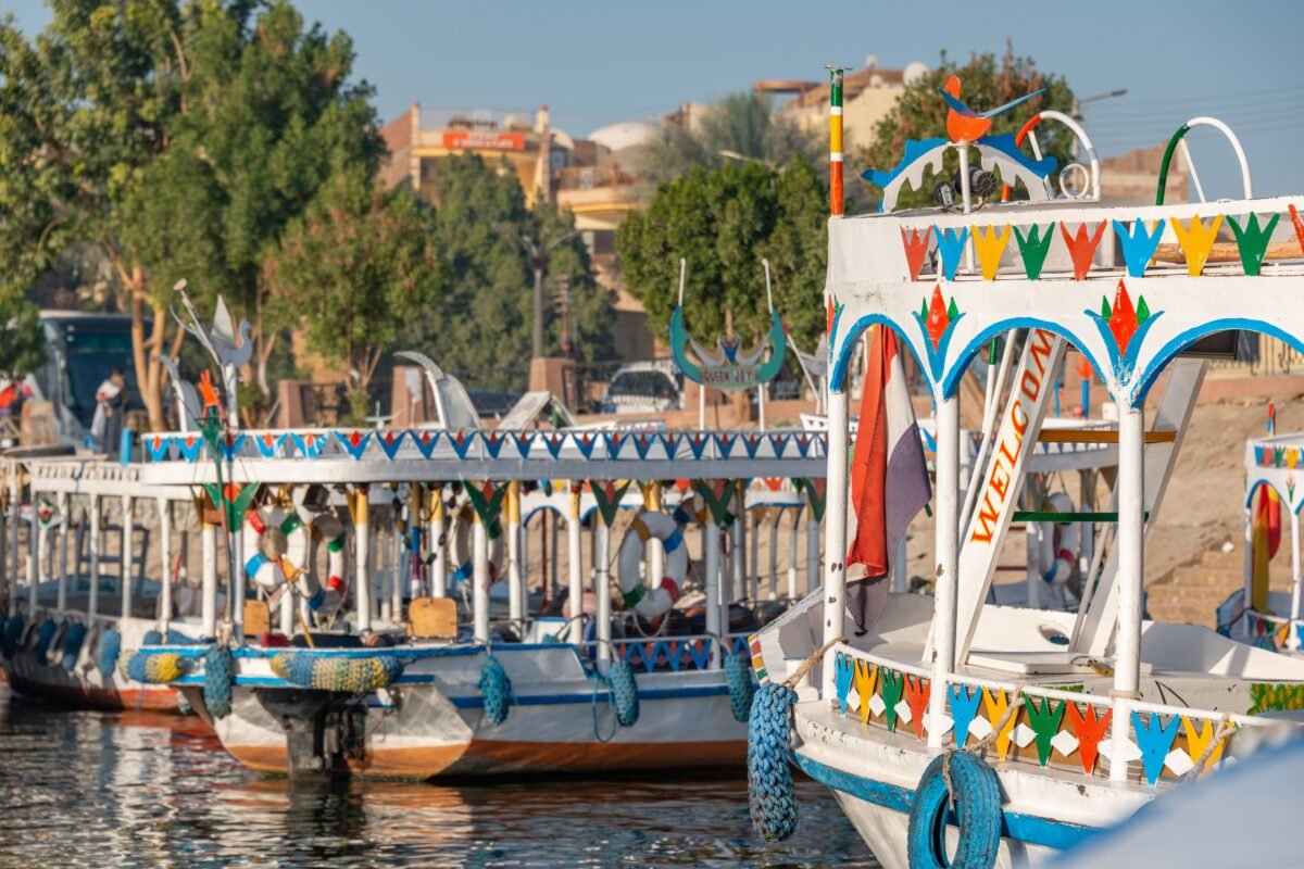 Vibrant traditional boats docked at Aswan harbor in Egypt, showcasing colorful designs and a lively atmosphere.