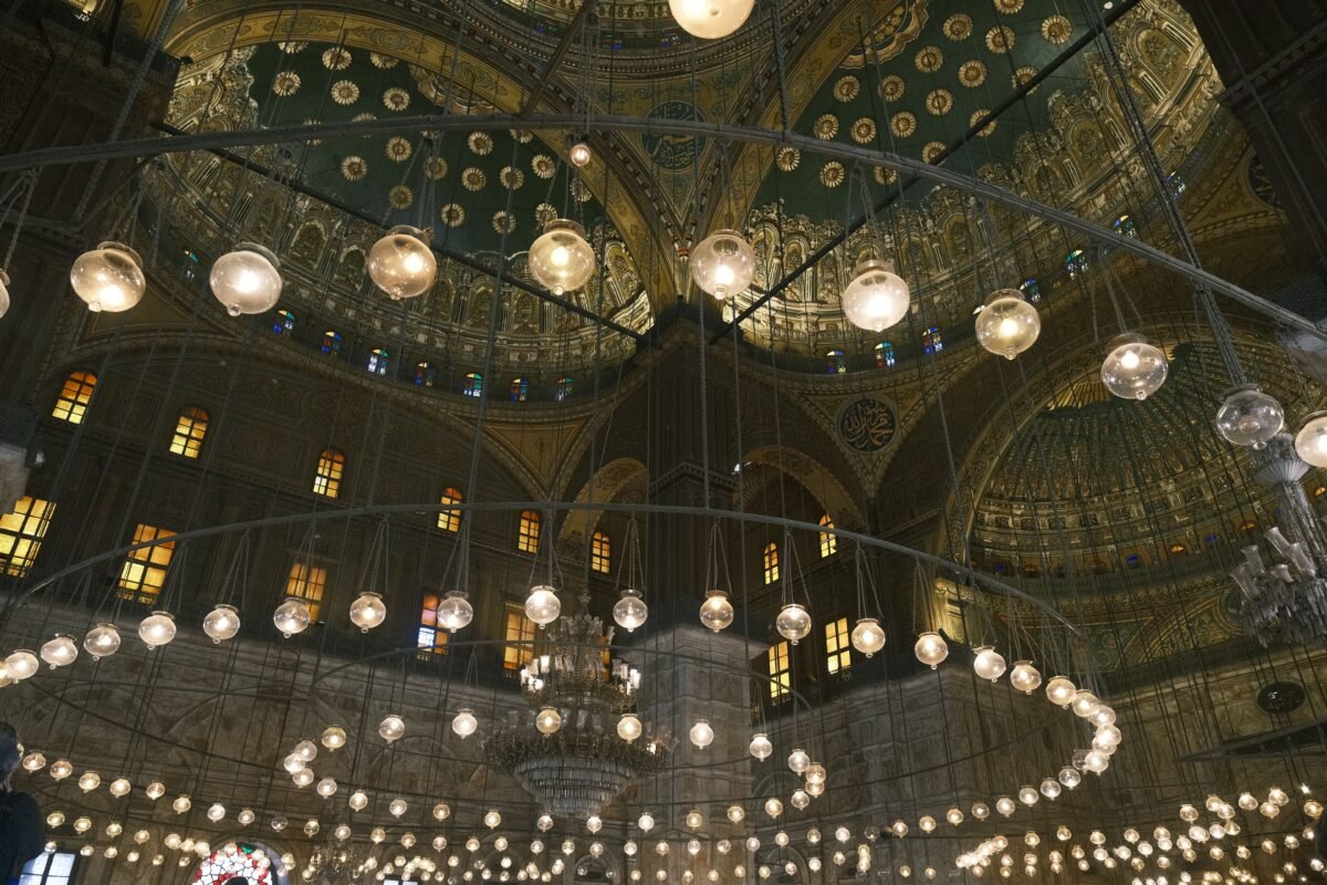 Interior view of a mosque showcasing an intricate dome and chandeliers.