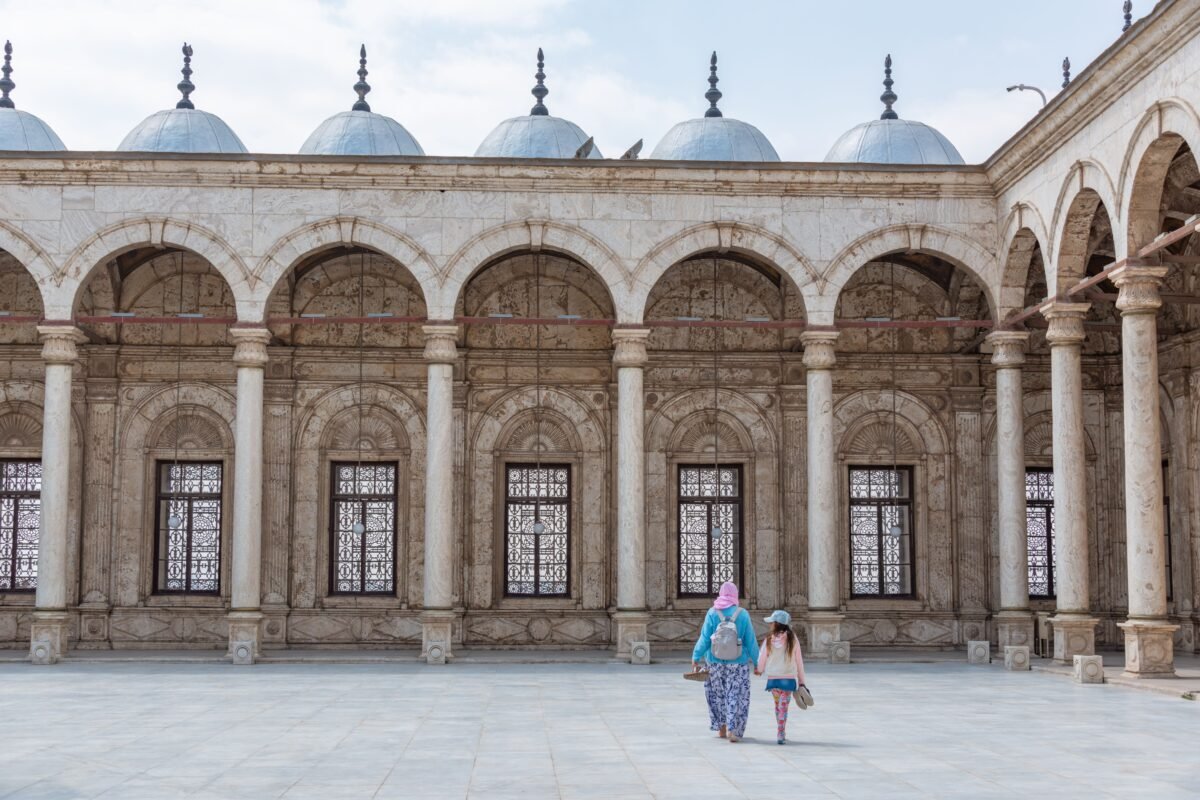 Two women walking in a historic mosque courtyard, highlighting traditional Islamic architecture.